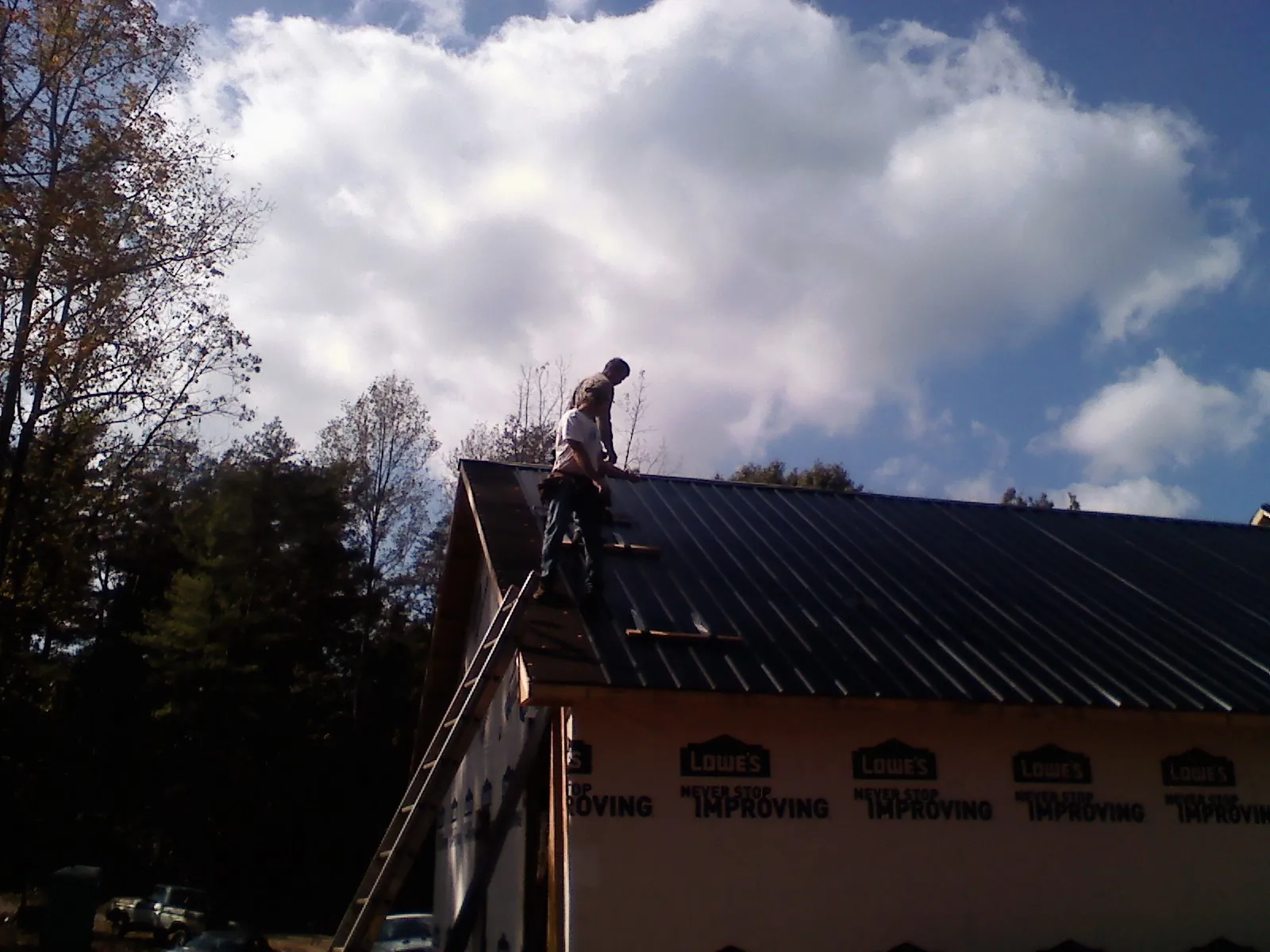 Roofer fastening dark metal panels high against a cloudy sky, from a Roof Inspection job in Sea Girt