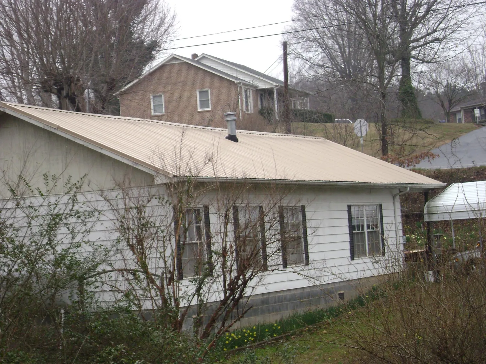 Tan metal roof on a white sided house set into a hillside — Commercial Roofing by Roofing Brothers in Sea Girt